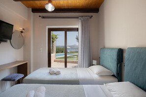 Ein Hotelzimmer mit zwei Betten, einem Fernseher, einem kleinen Tisch und Blick auf einen Pool und Berge.