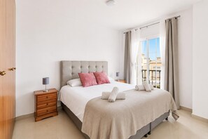 Een hotelkamer met een bed, nachtkastjes, uitzicht en een balkon.