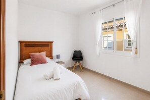 A hotel room with a wooden headboard bed, a black chair, a small bedside table with a lamp, and a window with curtains. - Villa Tropicana - Three Bedroom Villa, Sleeps 5 (Nerja)