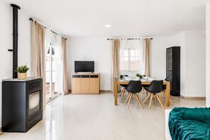 A modern living room with a fireplace, a dining area with a table and chairs, and a large window with curtains. - Villa Tropicana - Three Bedroom Villa, Sleeps 5 (Nerja)