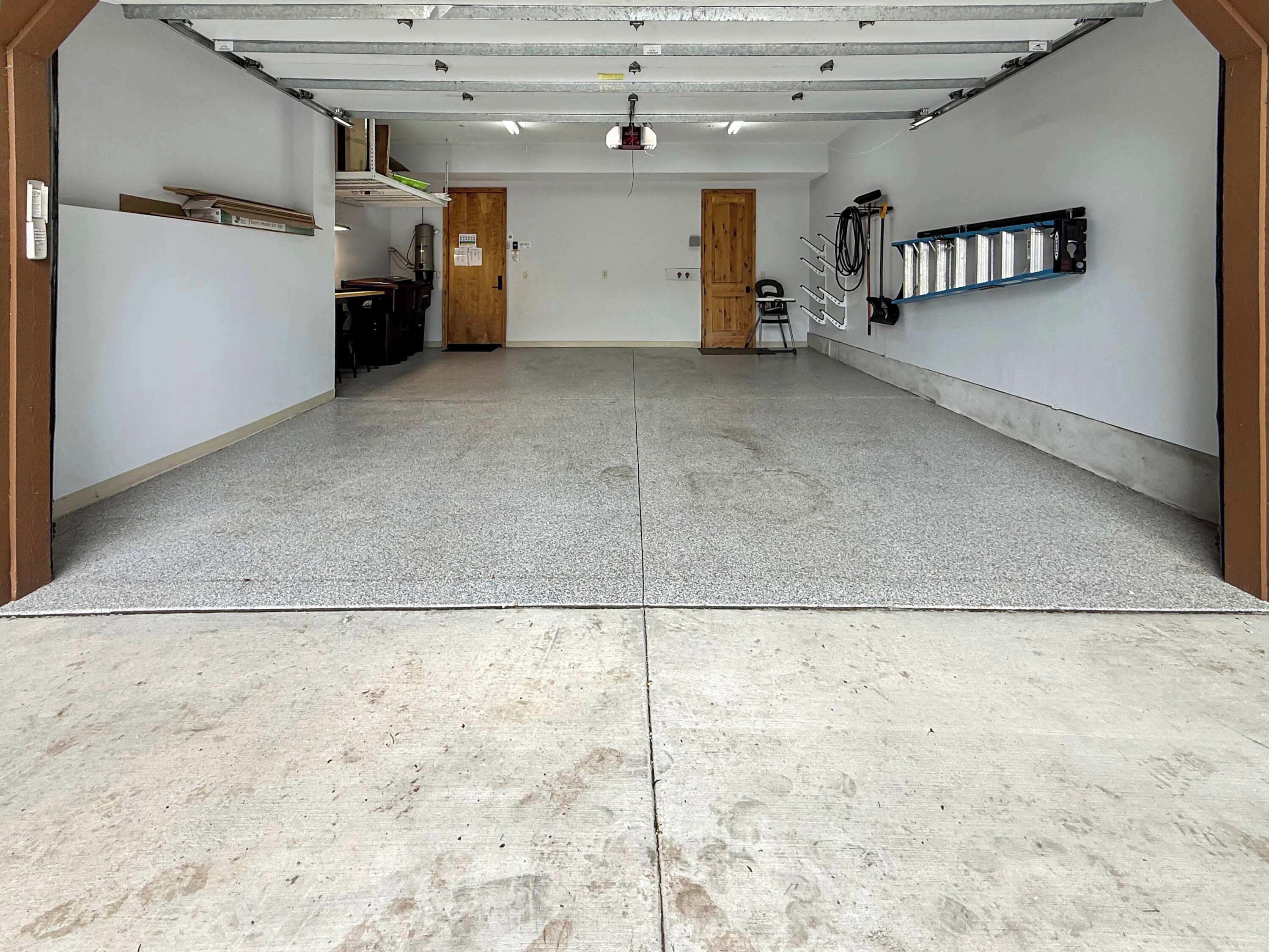 A spacious, well-lit indoor area with a concrete floor, a wooden door, and a metal rack on the wall.