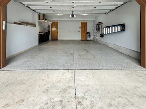 A spacious, well-lit indoor area with a concrete floor, a wooden door, and a metal rack on the wall.