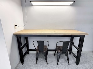Et lille arbejdsområde med et træbord, to stole, en stikkontakt og en lysarmatur.