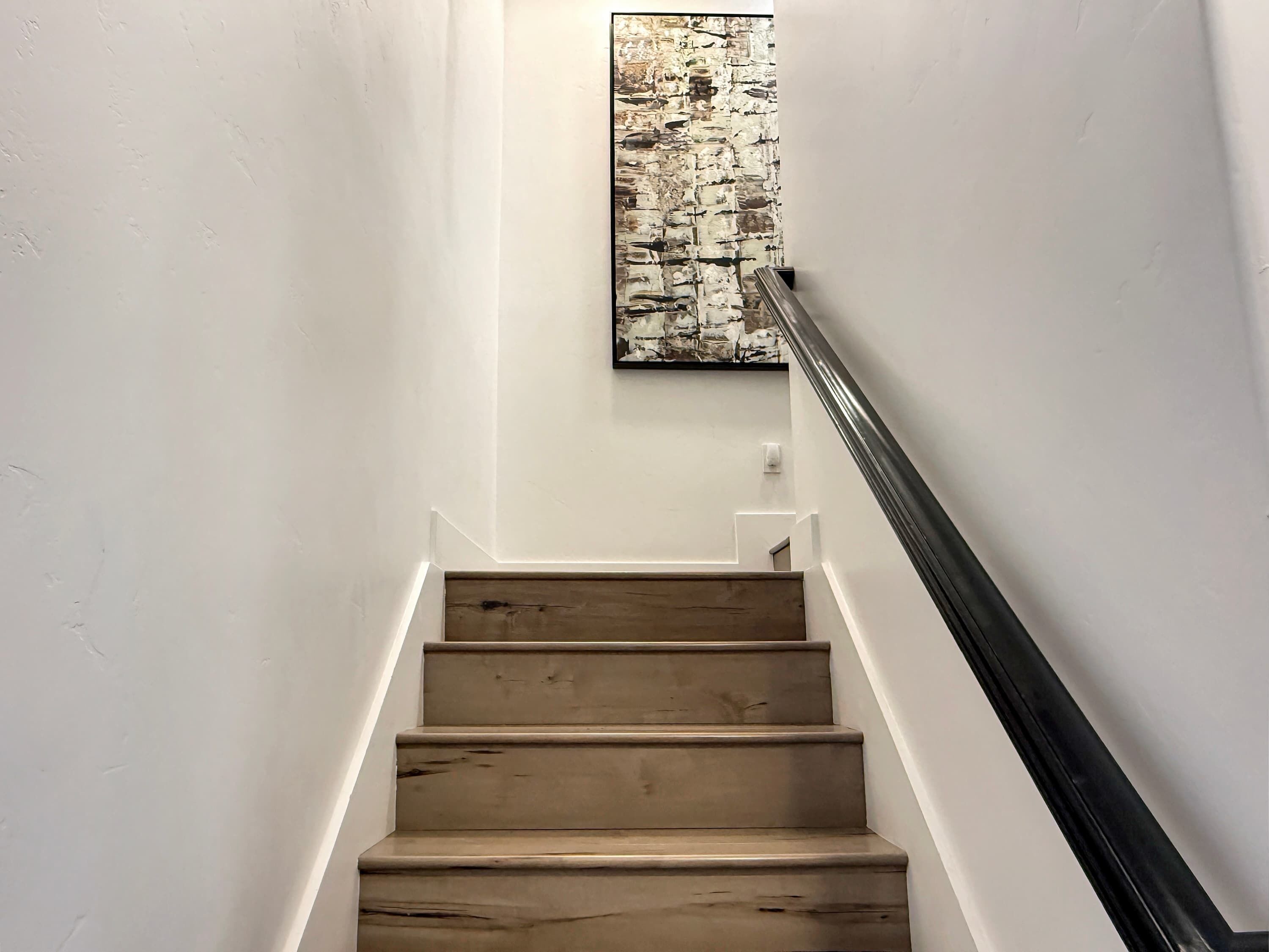 A staircase with wooden steps and a black handrail, leading to a landing with a textured wall art piece.