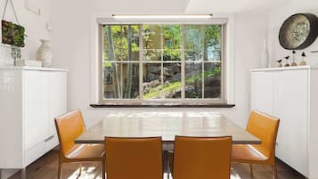 A dining area with a large window, white cabinetry, and two orange chairs.