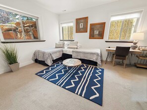 Een slaapkamer met een bed, een bureau, een stoel, een potplant en een vloerkleed.