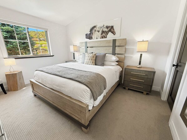 A bedroom with a large bed, bedside tables, a window, and a painting on the wall.