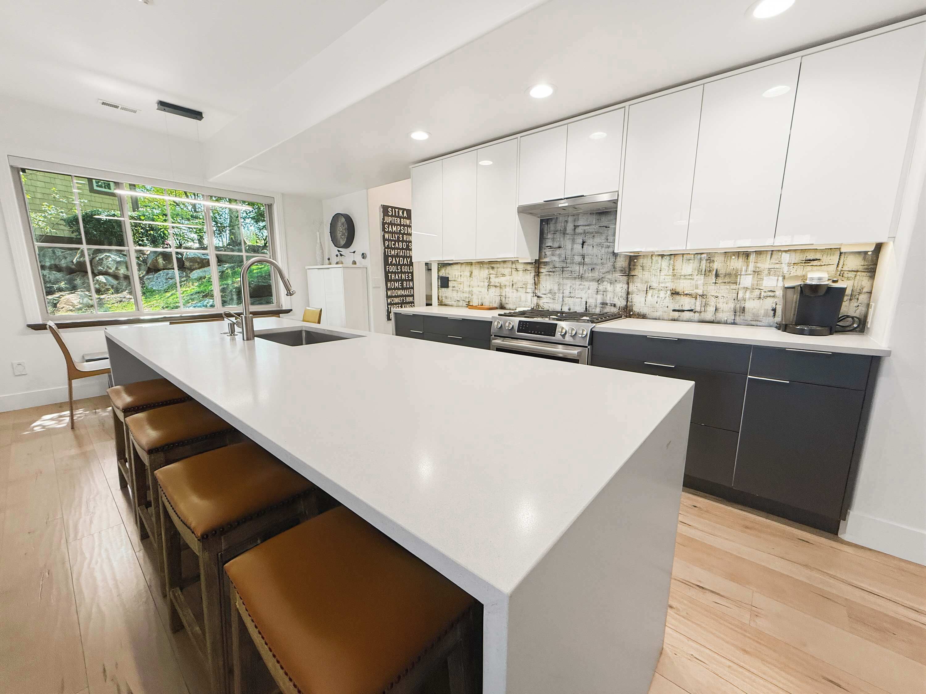 A modern kitchen with a large island, bar stools, and a view of greenery outside.