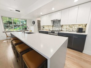 Een moderne keuken met een groot eiland, barstoelen en uitzicht op groen.