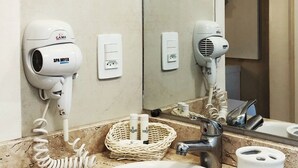 A bathroom with a marble sink, two wall-mounted hair dryers, a woven basket, and a mirror reflecting the room.