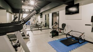 A gym with exercise equipment, a TV mounted on the wall, and a staircase leading to another level.
