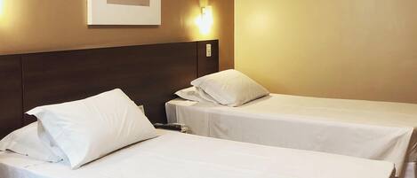 Habitación de hotel con dos camas individuales, cabecera, luz de pared y un cuadro enmarcado.