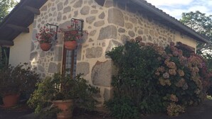 Ein Gebäude aus Stein mit geneigtem Dach, Blumentöpfen und einem kleinen Garten.