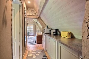 A narrow hallway leading to a bedroom with a bed and a chair, a kitchenette with a coffee maker, and a door leading to another room. - Romantic and Cozy Apartment in a Historic Farmhouse (Les Champeaux)