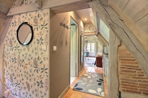 A hallway with patterned wallpaper, a mirror, and a rug leading to a staircase. - Romantic and Cozy Apartment in a Historic Farmhouse (Les Champeaux)