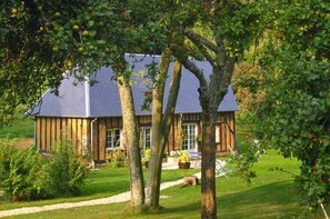 Ein rustikales Holzhaus mit geneigtem Dach, umgeben von einer gepflegten Rasenfläche und Obstbäumen.