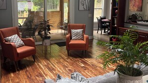 Un salón comedor amplio con suelo de madera, dos sillones, una mesa baja y una zona de comedor con mesa y sillas de madera.