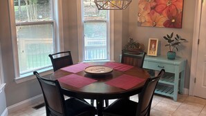 Un comedor con una mesa redonda, sillas, una lámpara colgante y un cuadro grande con motivos florales en la pared.