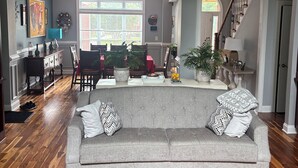 Un amplio salón con un sofá gris, piso de madera y una escalera que lleva a un nivel superior.