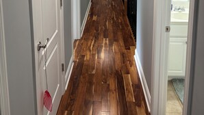 Un pasillo con suelo de madera, paredes blancas y puertas que dan a habitaciones.