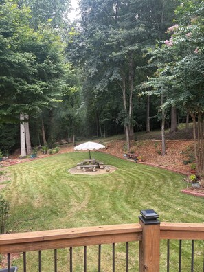 A backyard with a stone picnic table and umbrella, surrounded by trees and a well-maintained lawn.