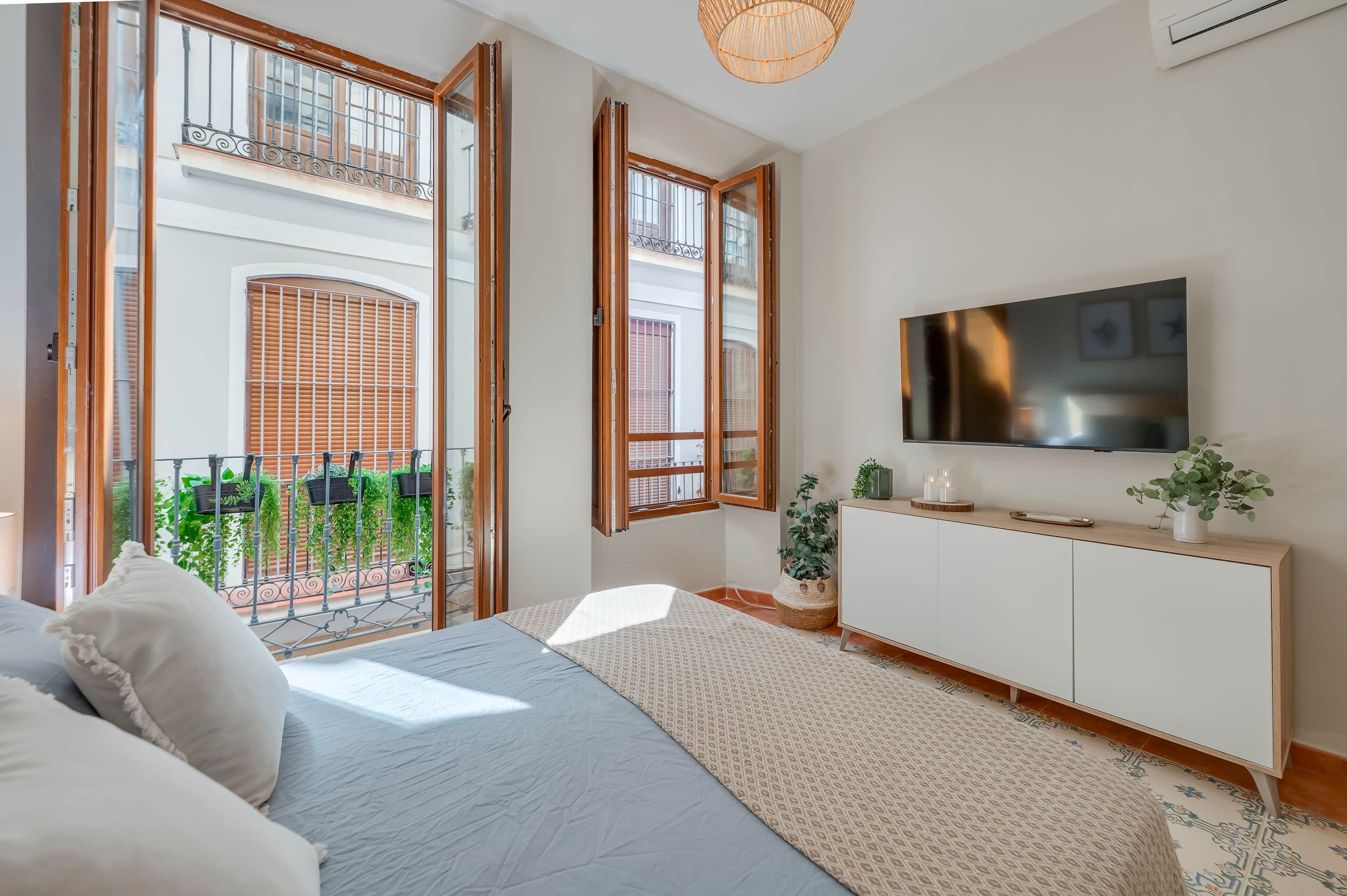 Une chambre à coucher comprenant un lit, un téléviseur, une console et un balcon agrémenté de plantes.