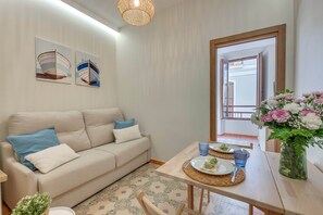 A modern living room with a sofa, a dining table with plates and glasses, and a vase of flowers. - Cozy and lovely apartment located in the historic center of Málaga. (Málaga)