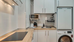 A compact kitchen with white cabinets, a microwave, a toaster, a coffee maker, a sink, and a washing machine. - Cozy and lovely apartment located in the historic center of Málaga. (Málaga)