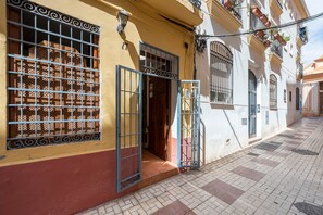 A building with a yellow facade, a metal gate, and a tiled pavement. - Cozy and lovely apartment located in the historic center of Málaga. (Málaga)