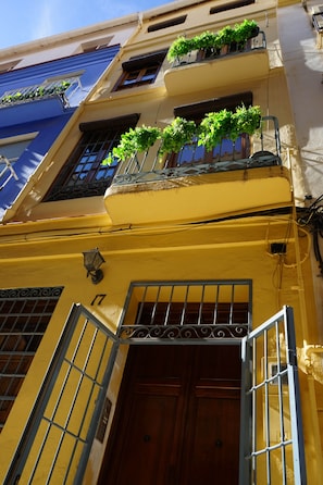 A yellow building with a wooden door, metal bars, and potted plants on the balcony. - Cozy and lovely apartment located in the historic center of Málaga. (Málaga)