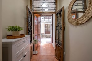 A narrow hallway with a wooden door leading to an outdoor area, a potted plant on a white cabinet, and a woven wall hanging. - Cozy and lovely apartment located in the historic center of Málaga. (Málaga)