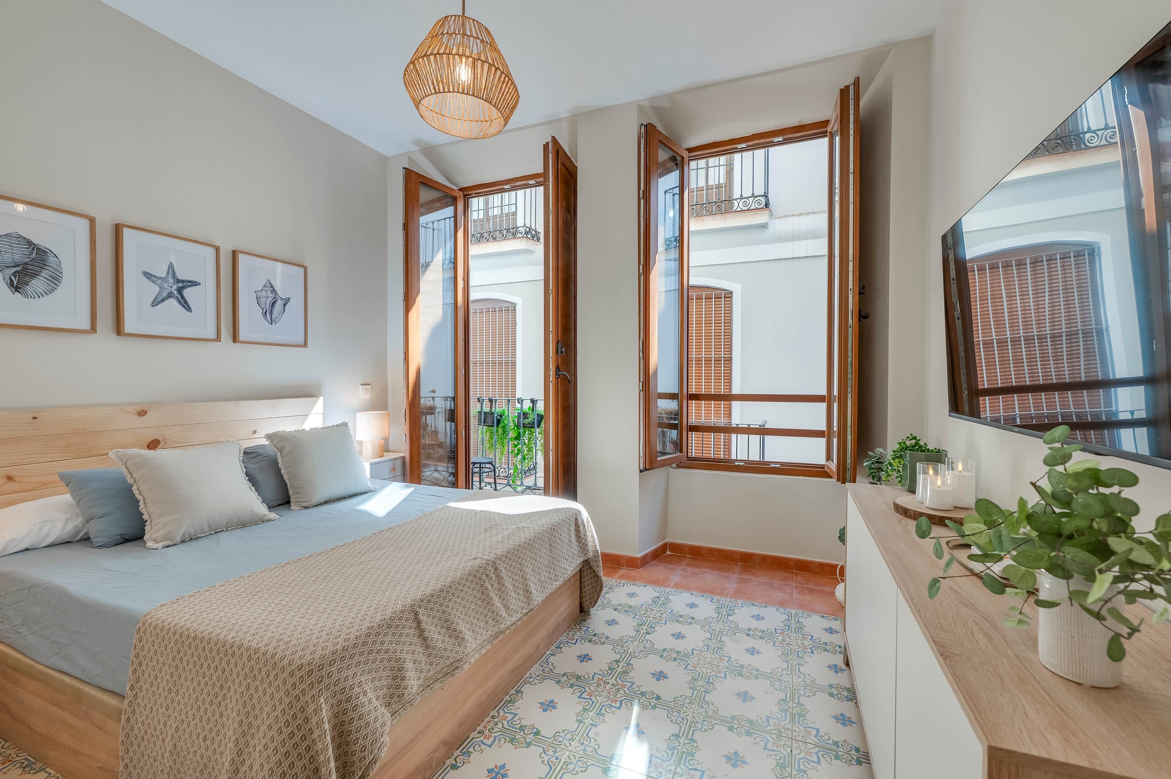 Une chambre à coucher avec un lit, une table de chevet ornée d’une plante et une fenêtre donnant sur l’extérieur.