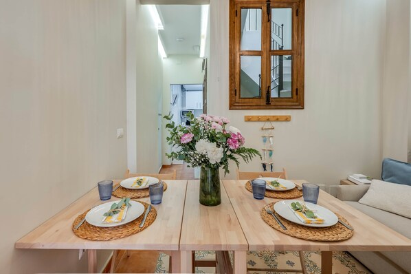 Une table à manger dressée avec des assiettes, des couverts et des verres bleus, et un vase rempli de fleurs placé au centre.