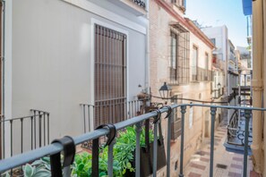 Une rue étroite, bordée de bâtiments des deux côtés, avec une rambarde en métal et quelques plantes.