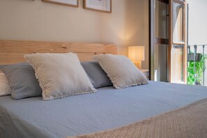 Ein Bett mit Holz Kopfteil, zwei Kissen und Blick auf einen Balkon mit Grünpflanzen.
