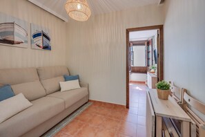 Ein Wohnzimmer mit einer Couch, einem Esstisch, einer Pendelleuchte und einer Tür zu einem anderen Raum.