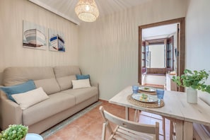 Ein Wohnzimmer mit Sofa, einem Esstisch mit Tellern und Gläsern sowie einer Pendelleuchte.