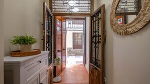 A narrow hallway with a wooden door leading to an outdoor area, a potted plant on a white cabinet, and a woven wall hanging. - Piso N°3 - Oliva Apartments Molinillo (Centro Histórico)