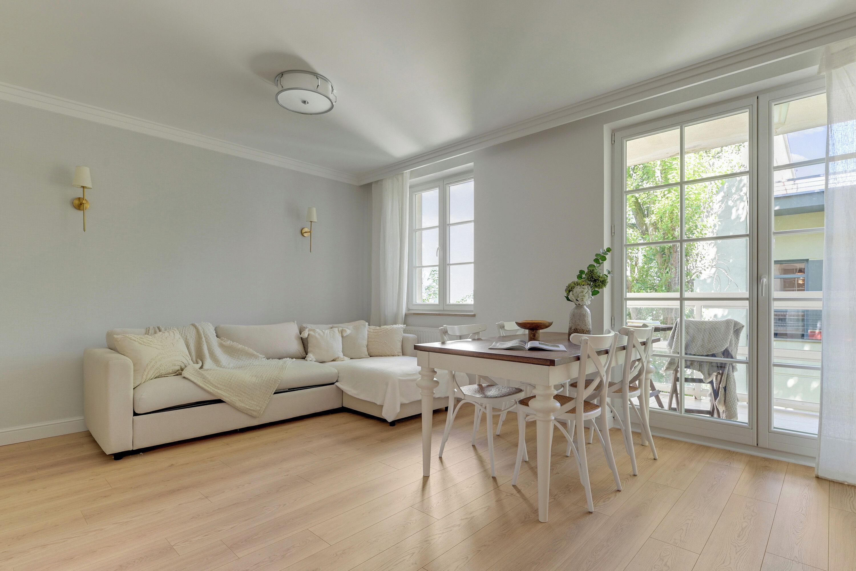Una sala de estar moderna con un sofá blanco, una mesa de comedor con sillas y ventanas amplias.