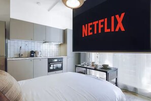 Une chambre d’hôtel équipée d’un lit, d’une kitchenette et d’un grand écran affichant le logo de Netflix.