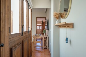Ein Flur mit Holztüren, ein Essbereich mit Tisch und Stühlen, ein Spiegel an der Wand und ein hängendes Ornament.