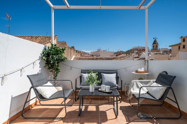 Una terraza en la azotea con una mesa, dos sillas, una planta en maceta y una pequeña mesa con velas.