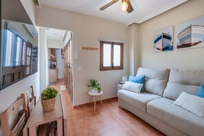 A living room with a sofa, a dining table with chairs, a kitchen in the background, and a ceiling fan. - Cozy and lovely apartment located in the historic center of Málaga. (Centro Histórico)
