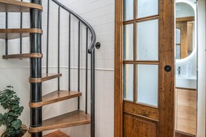 Gescalada de caragol amb graons de fusta i baranes metàl·liques, que porta a una habitació amb una porta de fusta i un mirall.