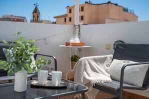Eine Dachterrasse mit einem Tisch für zwei Personen, einem Sessel mit Decke, einem Topfpflanzen und einem kleinen Tisch mit Kerzen und Korb.