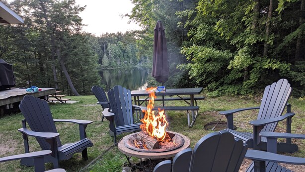 Um quintal com lareira, cadeiras Adirondack e mesa de piquenique.