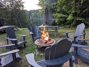 Ein Garten mit Feuerstelle, Adirondack-Stühlen und einem Picknicktisch.