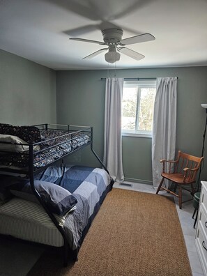 A bedroom with a bunk bed, a ceiling fan, a window with curtains, a wooden chair, and a desk with drawers. - Family friendly lakeside cottage. (Kearney)