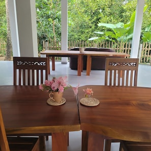 Une table à manger en bois, ornée de deux sets de table en fibres tressées, chacun supportant un petit vase contenant des fleurs roses. La table est entourée de chaises en bois dont les dossiers présentent des motifs complexes.