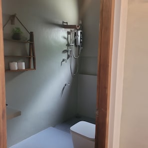 A small bathroom with a shower, toilet, and a shelf with toiletries.